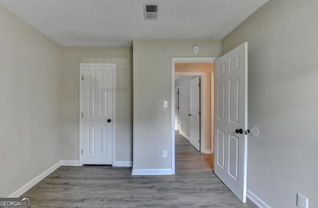 unfurnished bedroom featuring visible vents, baseboards, wood finished floors, and a closet