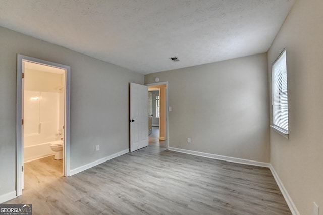 unfurnished bedroom featuring baseboards, connected bathroom, wood finished floors, and visible vents