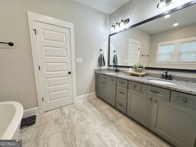 bathroom featuring baseboards, a soaking tub, double vanity, and a sink