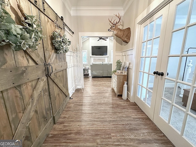 corridor featuring a decorative wall, wood finished floors, ornamental molding, a barn door, and wainscoting