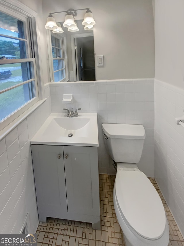 half bath with vanity, visible vents, toilet, tile walls, and a wainscoted wall