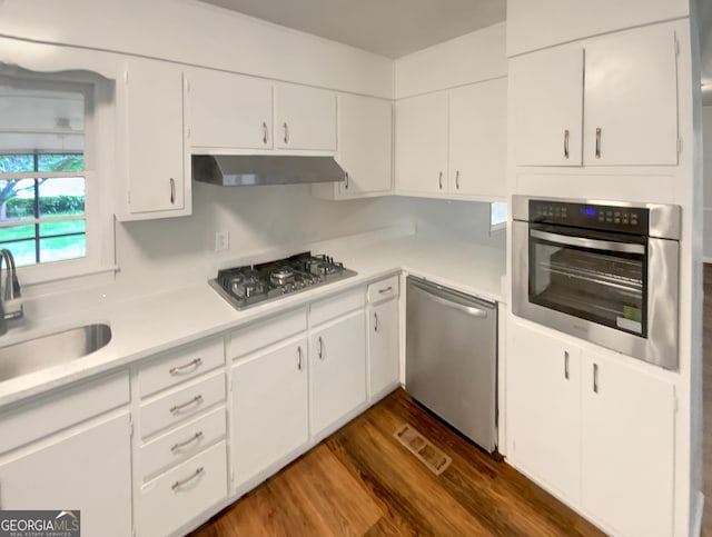 kitchen featuring light countertops, under cabinet range hood, a sink, dark wood finished floors, and stainless steel appliances