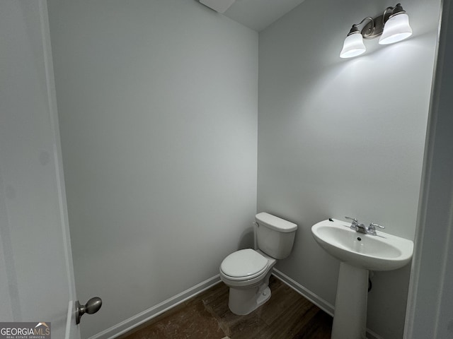 half bathroom with a sink, baseboards, toilet, and wood finished floors
