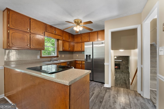 kitchen featuring brown cabinetry, a peninsula, stainless steel fridge, a sink, and dark wood finished floors
