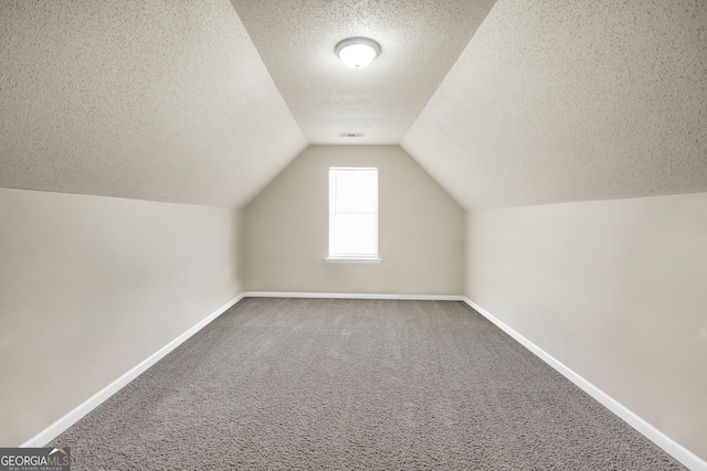 additional living space with carpet floors, a textured ceiling, vaulted ceiling, and baseboards