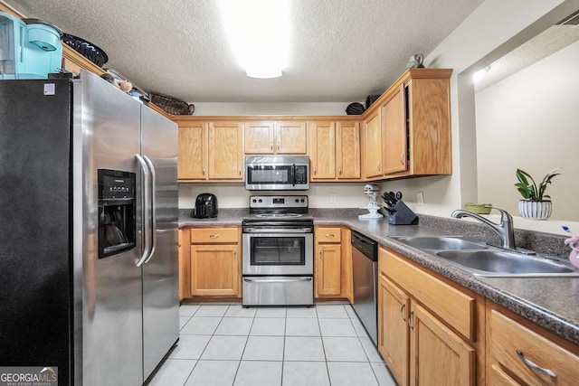 kitchen with dark countertops, appliances with stainless steel finishes, a sink, a textured ceiling, and light tile patterned floors