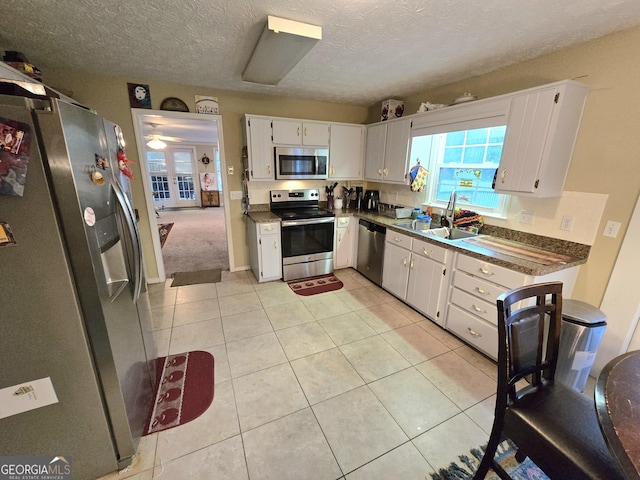 kitchen with dark countertops, a sink, light tile patterned floors, white cabinets, and stainless steel appliances