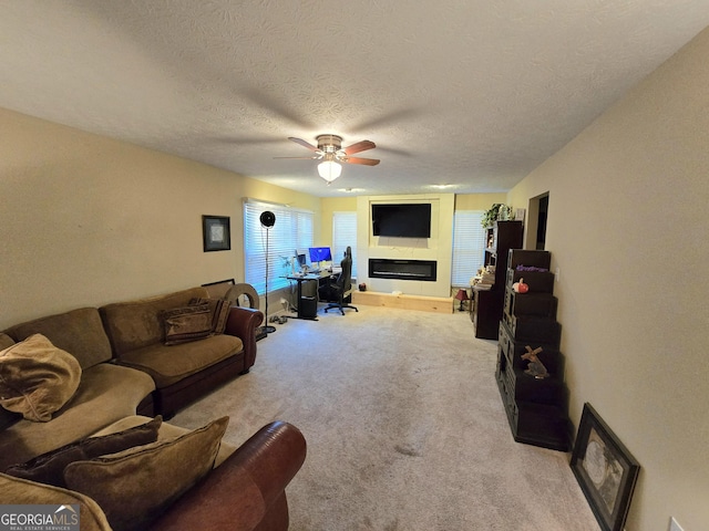 carpeted living area with a ceiling fan, a textured ceiling, and a glass covered fireplace