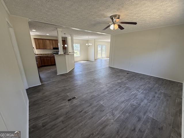 unfurnished living room featuring a textured ceiling, ceiling fan with notable chandelier, ornate columns, visible vents, and dark wood-style floors