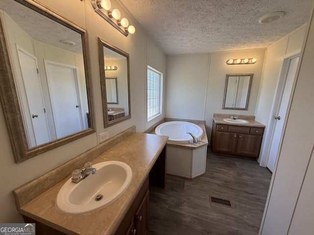 bathroom with a textured ceiling, visible vents, a sink, and wood finished floors