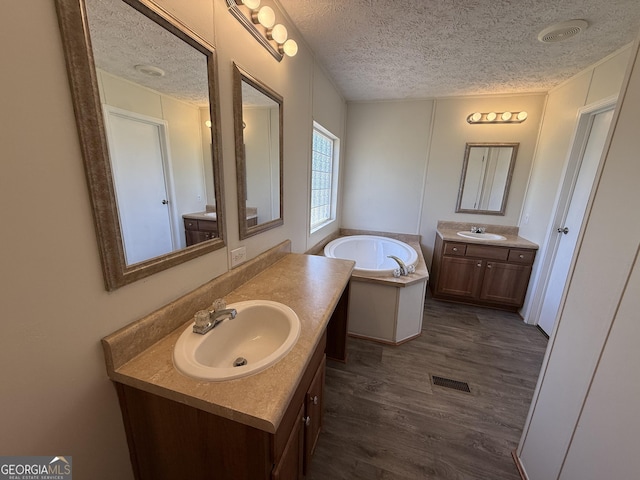 full bath featuring a textured ceiling, visible vents, a sink, and wood finished floors