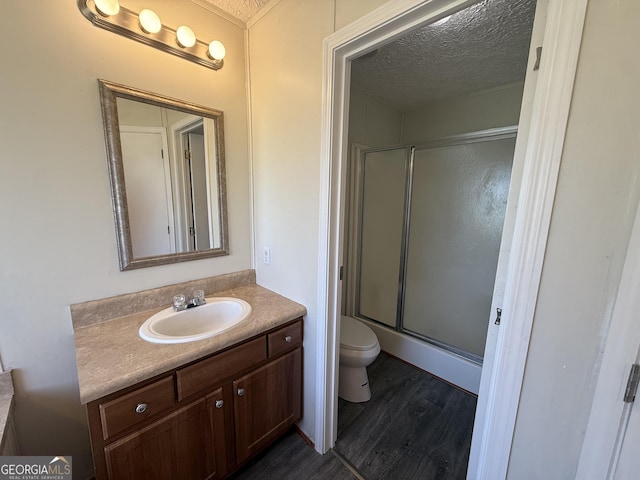 bathroom featuring a shower with shower door, vanity, toilet, a textured ceiling, and wood finished floors