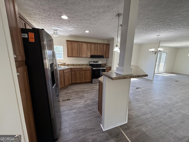 kitchen with a sink, appliances with stainless steel finishes, brown cabinetry, and dark wood-type flooring