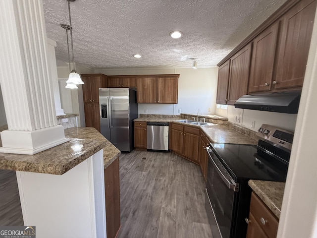 kitchen with brown cabinetry, wood finished floors, a sink, under cabinet range hood, and stainless steel appliances