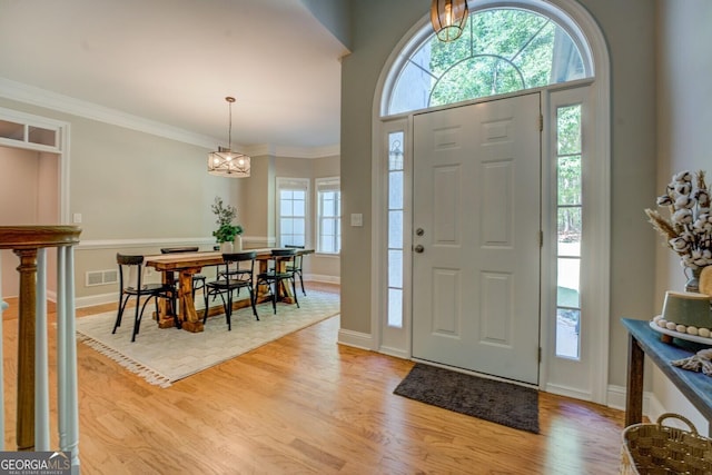 entryway with light wood-style floors, a chandelier, baseboards, and ornamental molding