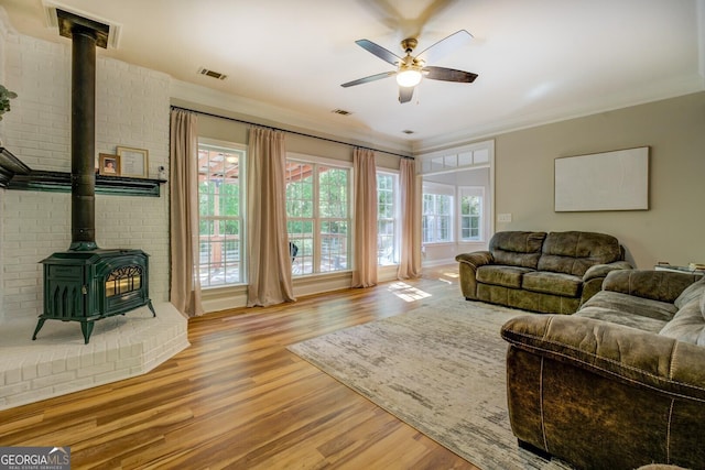 living area with a wood stove, wood finished floors, a ceiling fan, and ornamental molding