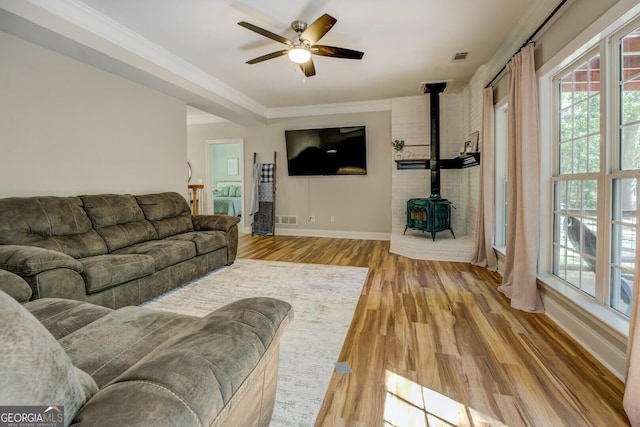 living room featuring a wood stove, ceiling fan, light wood-type flooring, baseboards, and ornamental molding