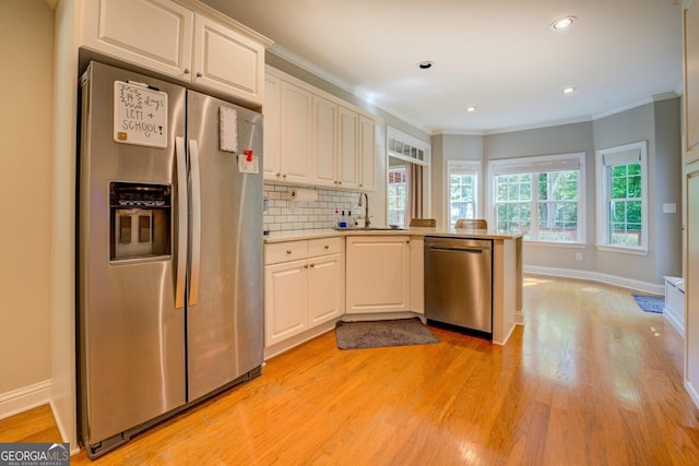 kitchen featuring stainless steel appliances, a peninsula, light wood finished floors, light countertops, and ornamental molding