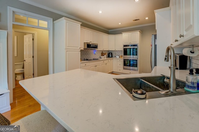 kitchen with appliances with stainless steel finishes, a sink, crown molding, light wood finished floors, and backsplash