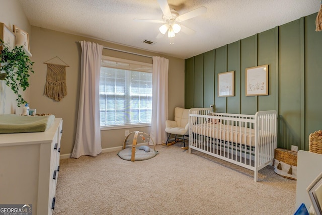 bedroom featuring a crib, carpet flooring, a ceiling fan, a textured ceiling, and baseboards