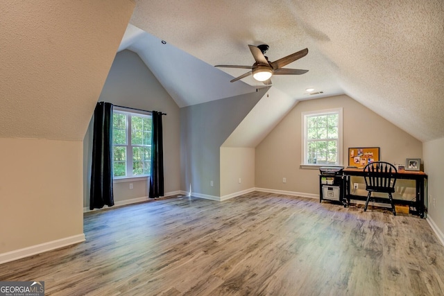 additional living space with ceiling fan, wood finished floors, healthy amount of natural light, lofted ceiling, and a textured ceiling
