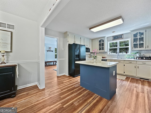 kitchen featuring visible vents, a textured ceiling, a sink, light wood finished floors, and black appliances