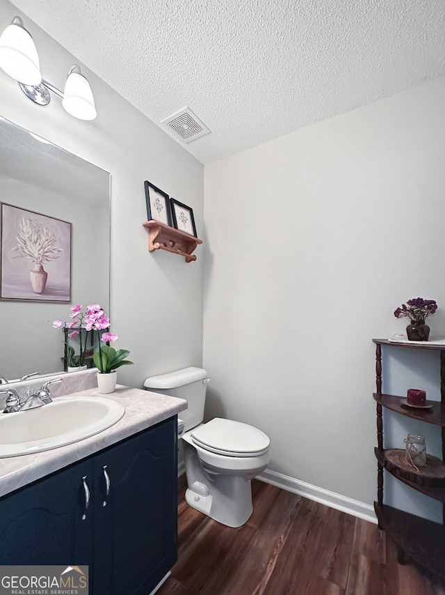 half bath featuring vanity, visible vents, wood finished floors, toilet, and a textured ceiling