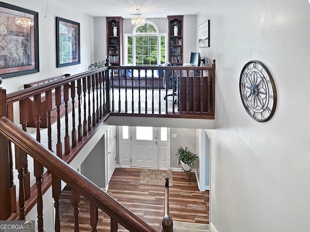 stairs with baseboards, a textured ceiling, wood finished floors, and a notable chandelier