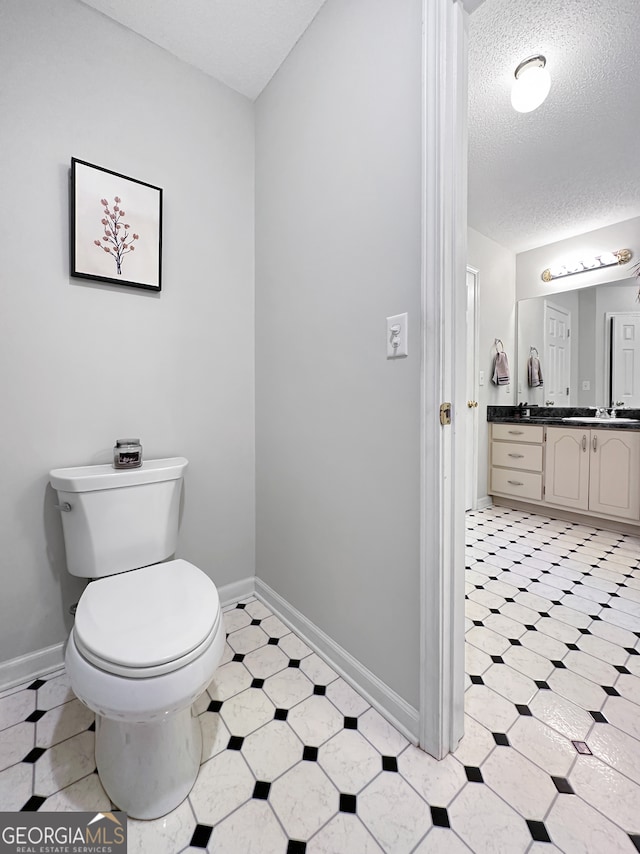 bathroom with vanity, toilet, baseboards, a textured ceiling, and tile patterned floors