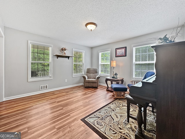 sitting room with baseboards, visible vents, a textured ceiling, and wood finished floors