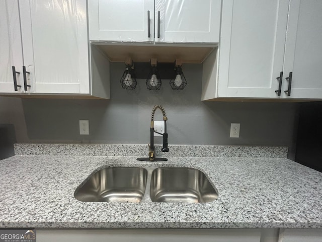 room details featuring light stone counters, a sink, and white cabinets