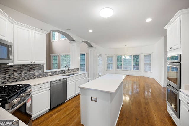 kitchen with a kitchen island, appliances with stainless steel finishes, arched walkways, a sink, and ornate columns