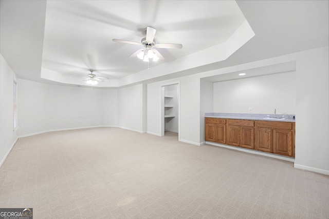 unfurnished living room with light carpet, baseboards, a tray ceiling, a sink, and wet bar