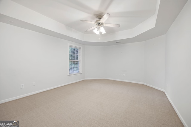 empty room featuring a ceiling fan, baseboards, light colored carpet, and a tray ceiling