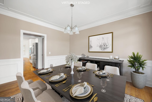 dining area featuring crown molding, a wainscoted wall, an inviting chandelier, and wood finished floors