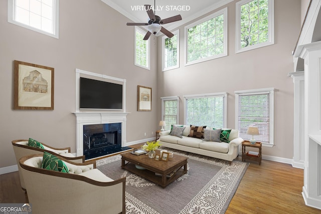1382 Benbrooke Ln NW, Acworth, GA 30101 - living room with a fireplace with raised hearth, a ceiling fan, a towering ceiling, wood finished floors, and crown molding