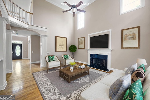 living room with ornate columns, a ceiling fan, wood finished floors, and a towering ceiling