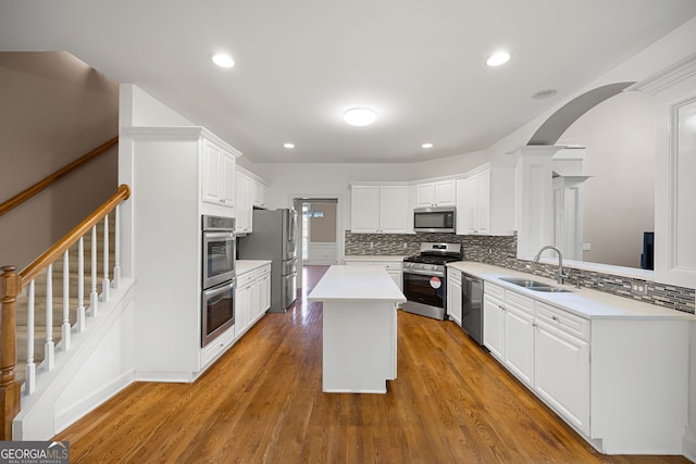 kitchen with a sink, arched walkways, tasteful backsplash, and stainless steel appliances