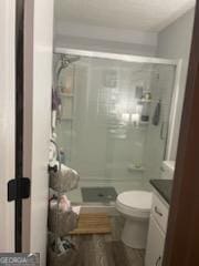bathroom with wood finished floors, a stall shower, toilet, and vanity