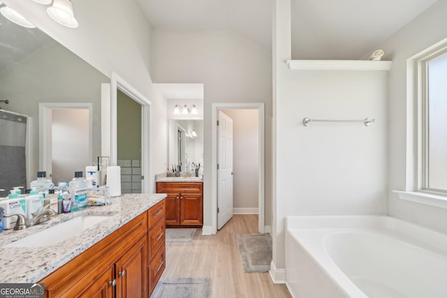 bathroom with a sink, two vanities, wood finished floors, lofted ceiling, and a bath