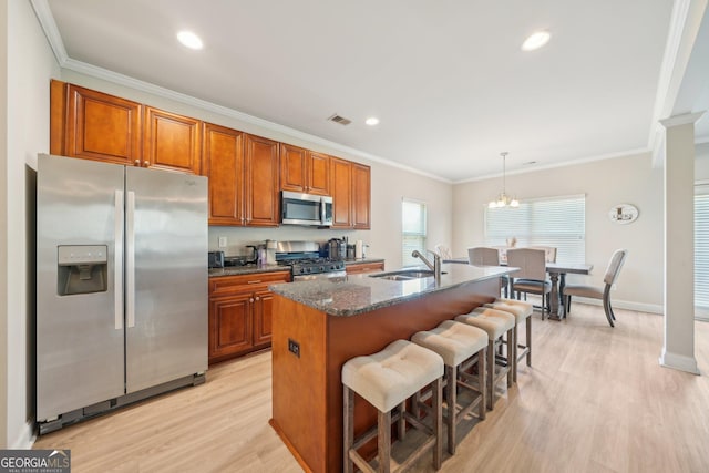 kitchen featuring visible vents, a kitchen island with sink, light wood-type flooring, brown cabinets, and appliances with stainless steel finishes