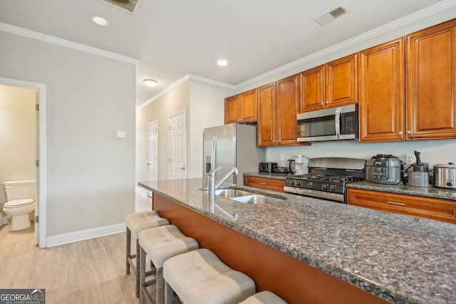 kitchen featuring a sink, dark stone counters, stainless steel appliances, a kitchen bar, and visible vents