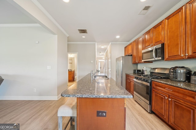 kitchen with a kitchen breakfast bar, light wood-style flooring, a sink, dark stone countertops, and appliances with stainless steel finishes