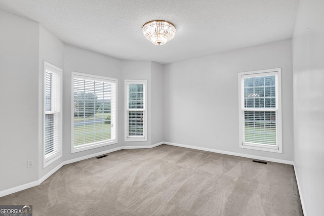 carpeted empty room with an inviting chandelier, visible vents, baseboards, and a healthy amount of sunlight