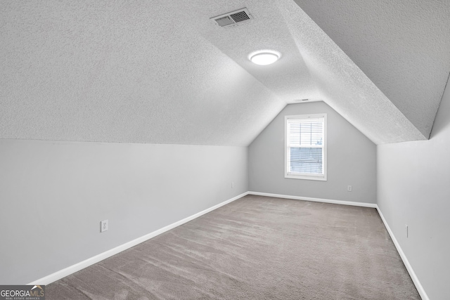 additional living space with a textured ceiling, visible vents, vaulted ceiling, carpet floors, and baseboards