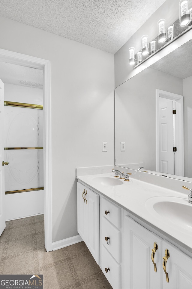full bathroom with double vanity, a textured ceiling, baseboards, and a sink