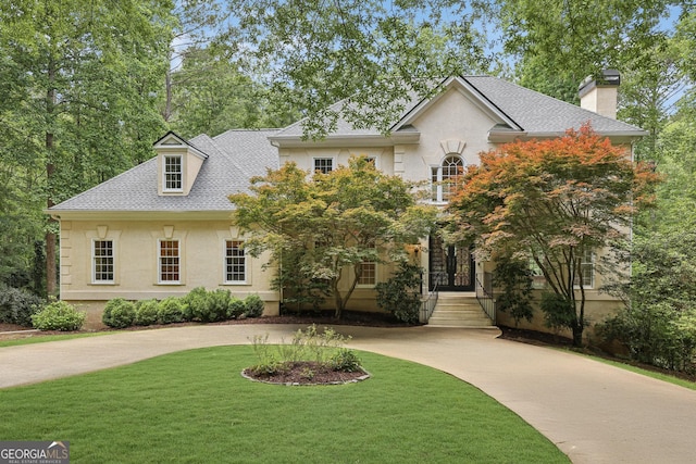 view of front facade featuring a chimney, curved driveway, a front yard, and roof with shingles