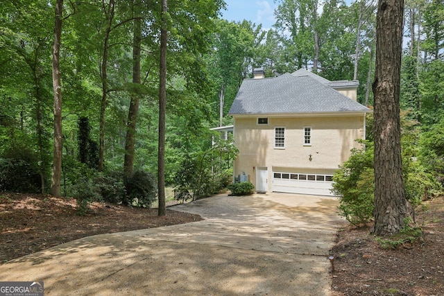 view of side of property with stucco siding, driveway, a chimney, a garage, and roof with shingles