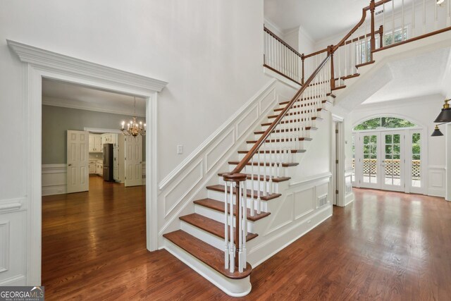 stairs featuring a decorative wall, a chandelier, crown molding, wood finished floors, and a towering ceiling