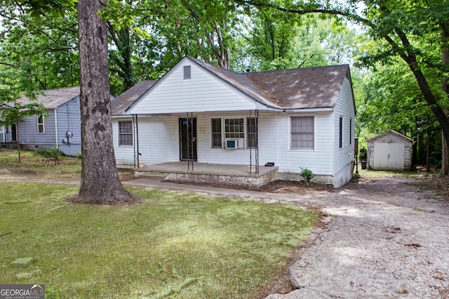 bungalow-style home featuring an outdoor structure, a shingled roof, a shed, and covered porch